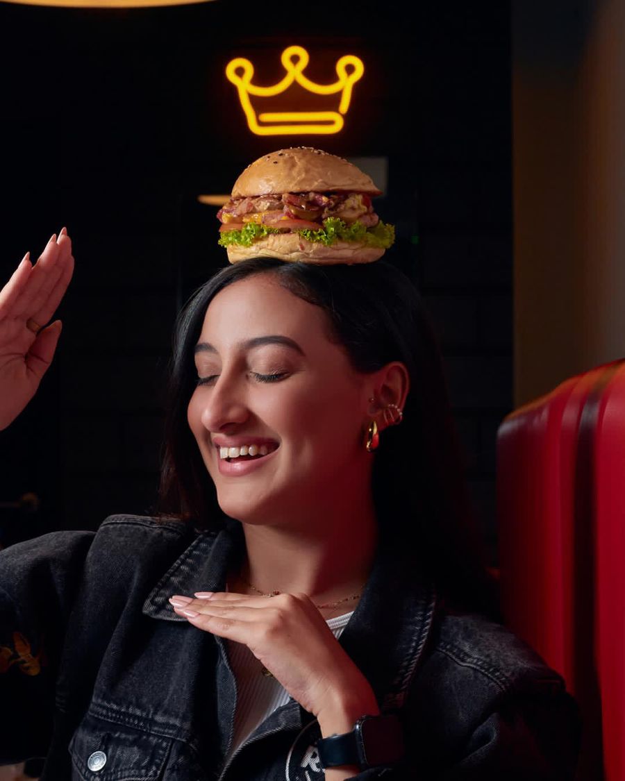 Smiling woman with a burger on her head under a neon crown