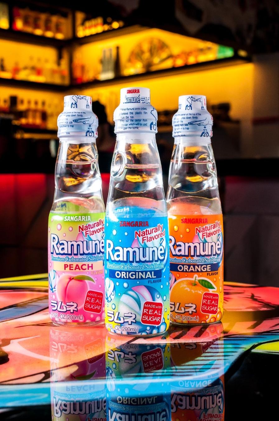 Three bottles of Ramune on a bar with colorful lights