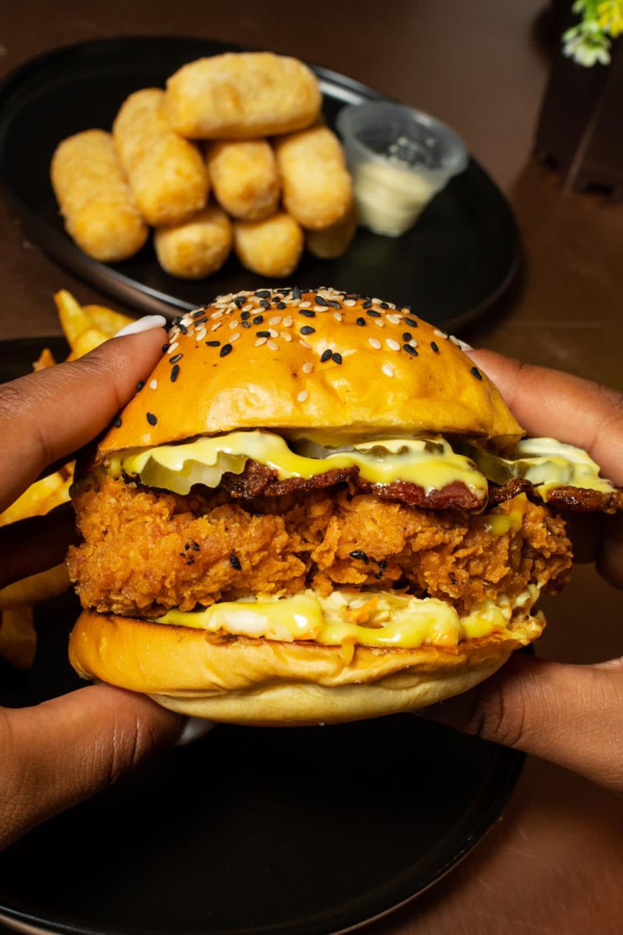 Hands holding a fried chicken burger with cheese