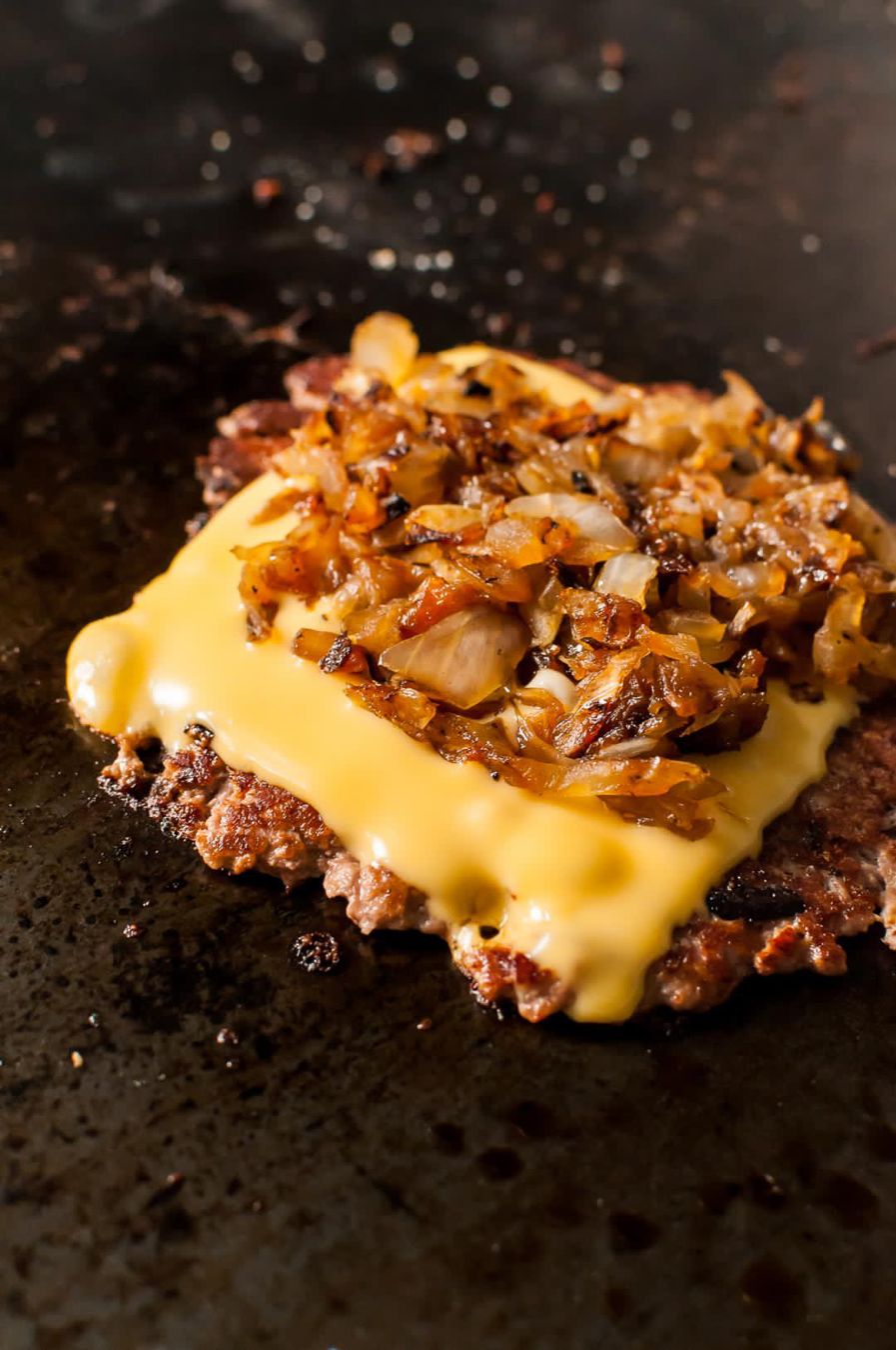 Smash burger with melted cheese and caramelized onions on the griddle